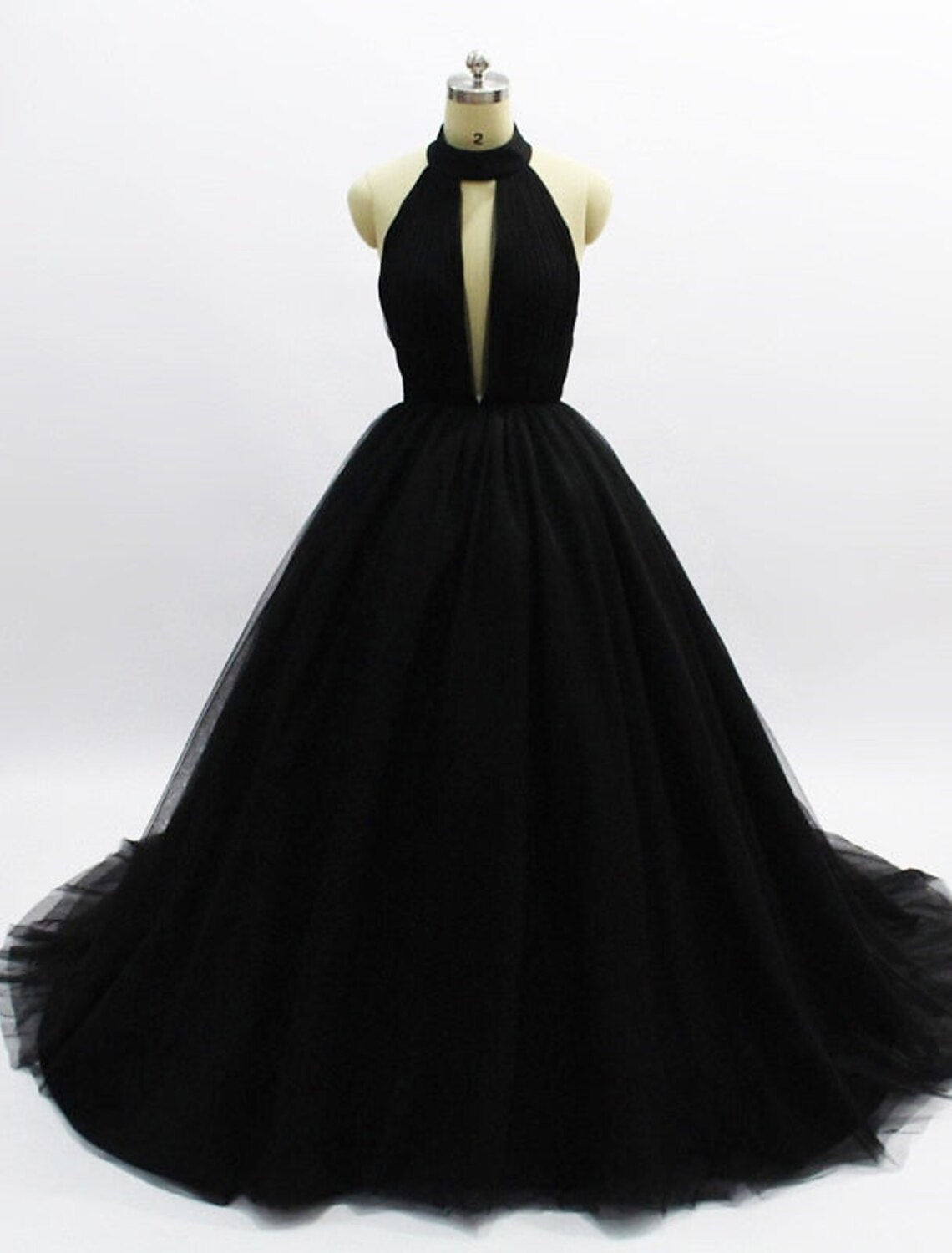 Model wearing an elegant halter ball gown prom dress with an open back and tulle pleats.